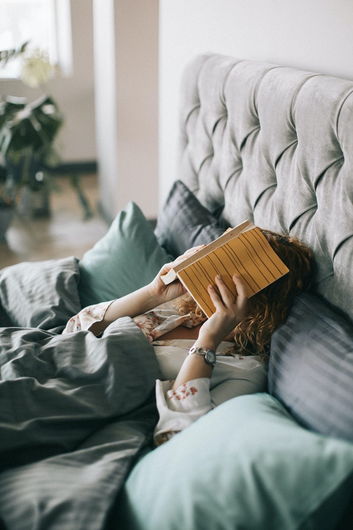 woman-covering-face-with-book-on-bed