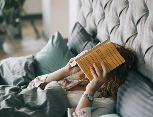 woman-covering-face-with-book-on-bed